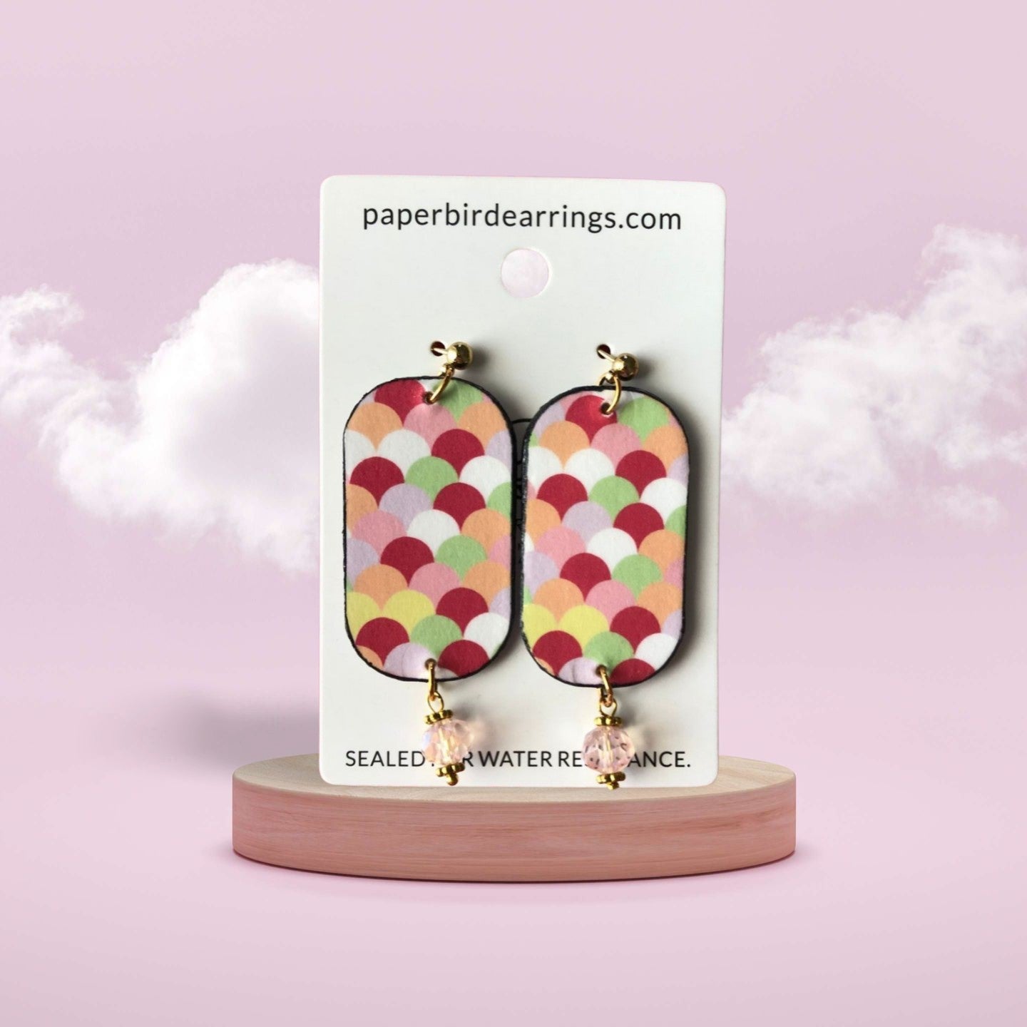 Colorful patterned earrings on a branded card with a pink background