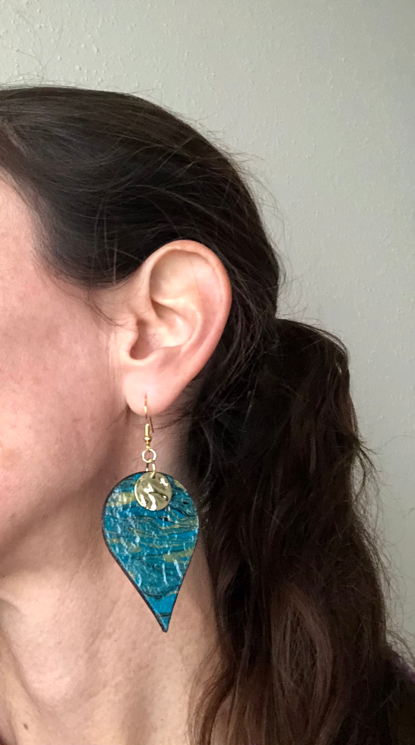 Person wearing a blue teardrop earring with a gold accent.