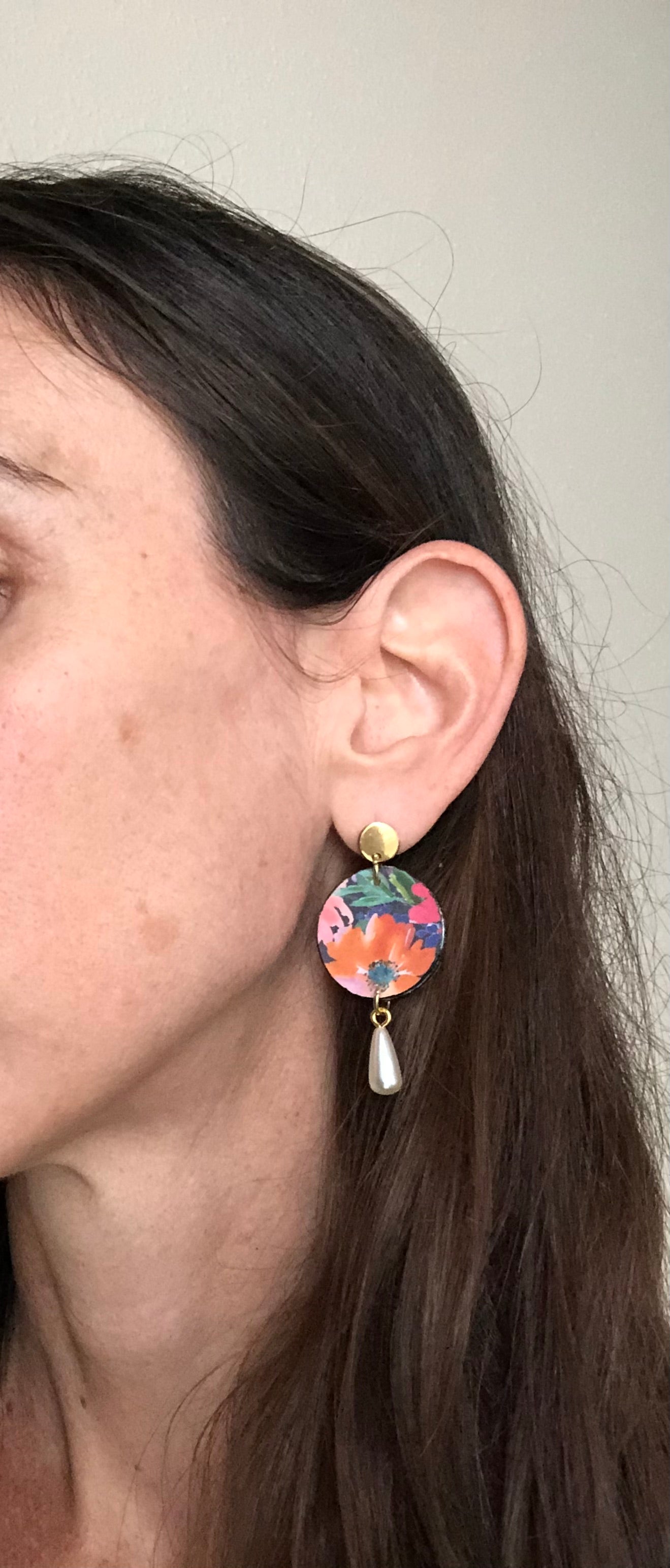 Close-up of a person wearing colorful earrings with a neutral background