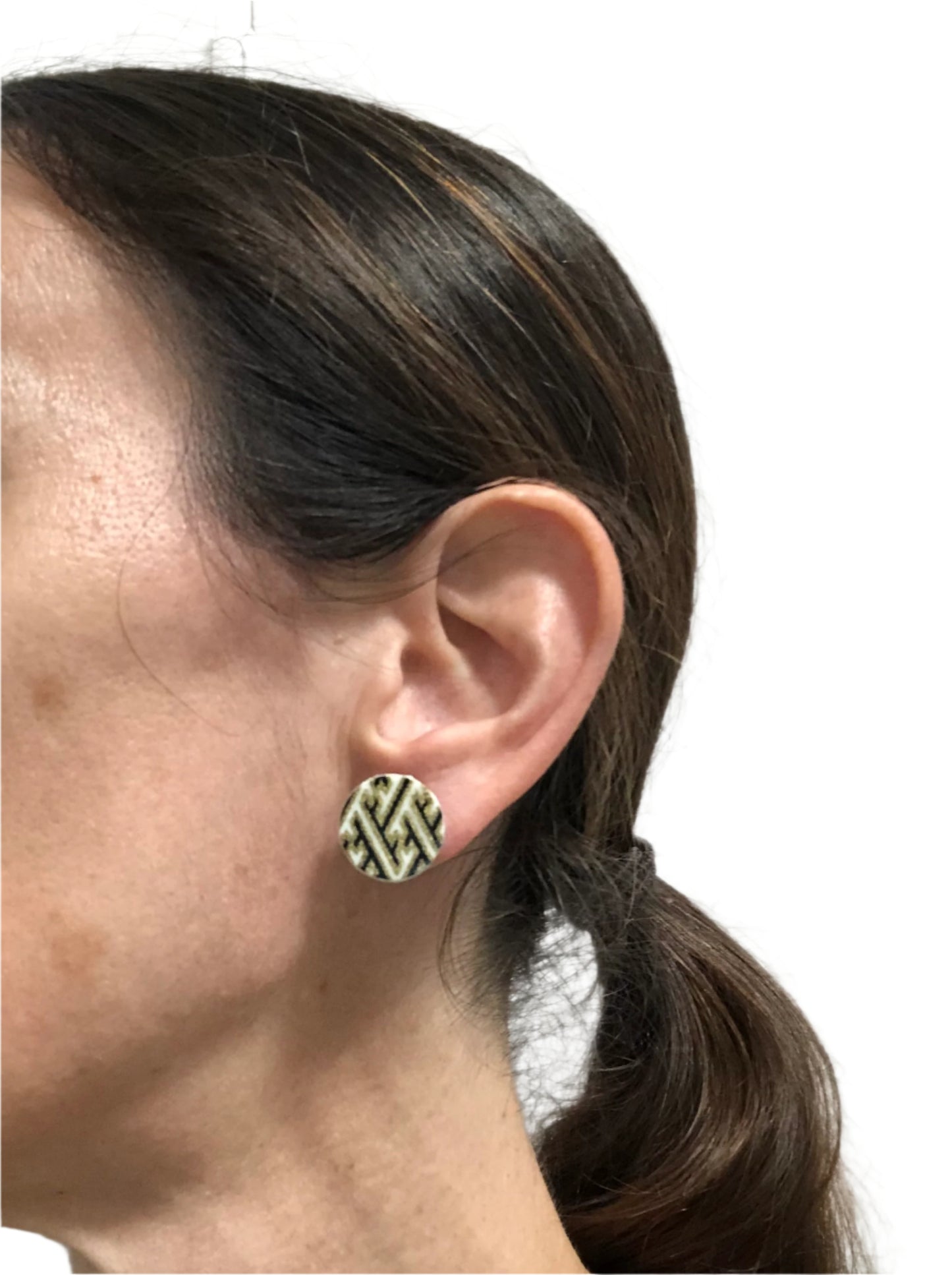 Close-up of an ear wearing a geometric patterned earring against a neutral background