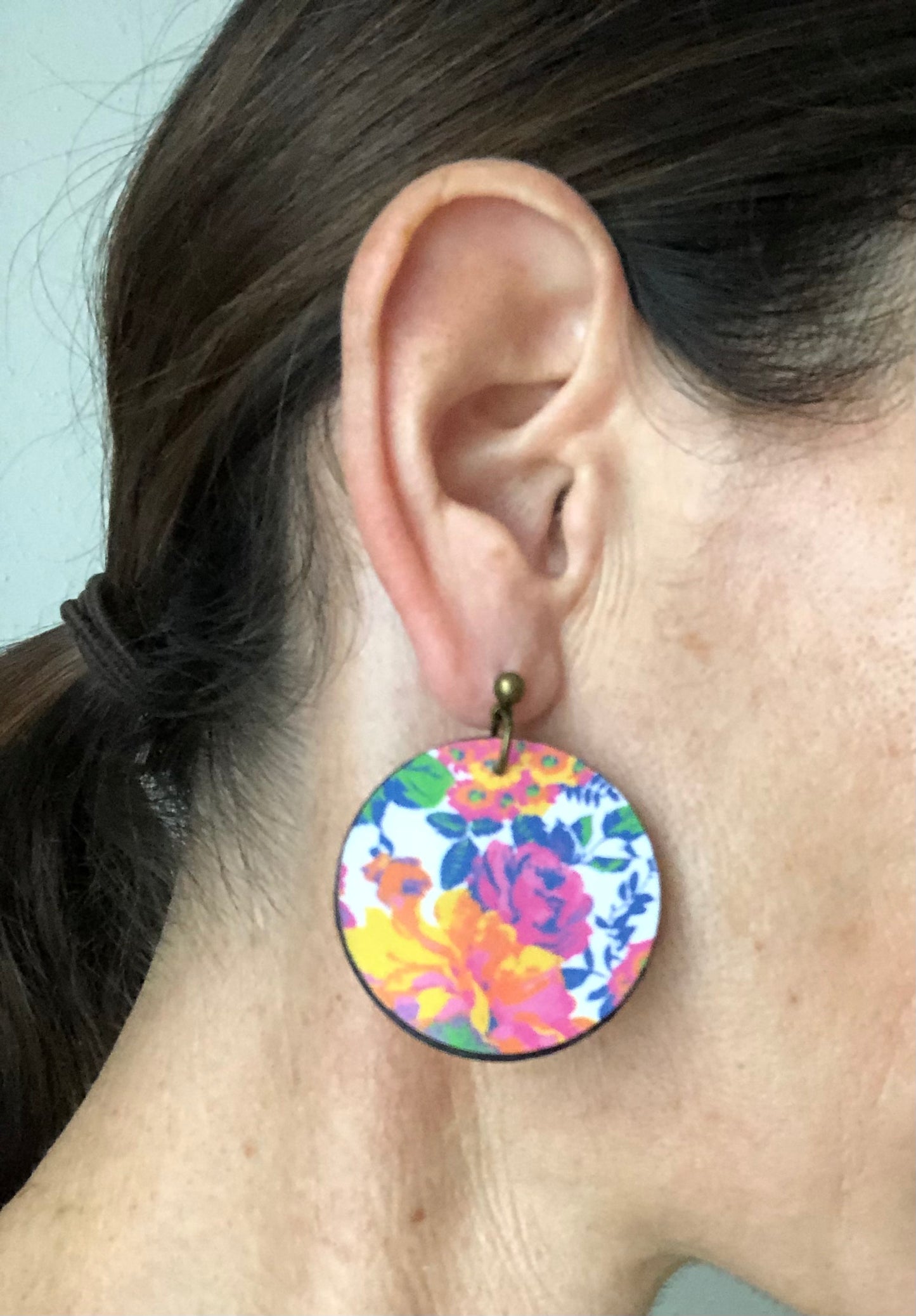 Close-up of a colorful floral earring worn by a person with hair in a ponytail.