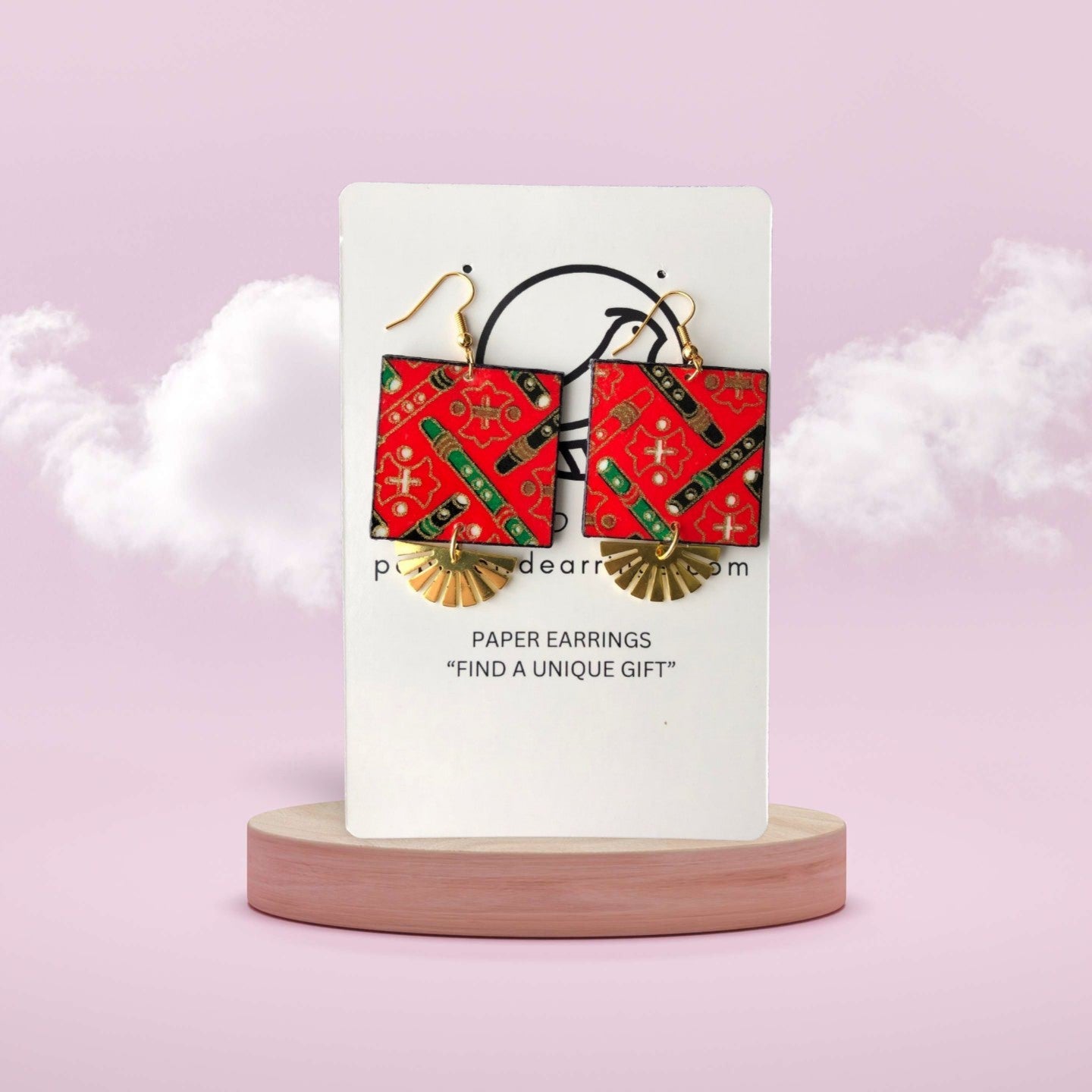 Red and gold paper earrings on a white card with a pink background