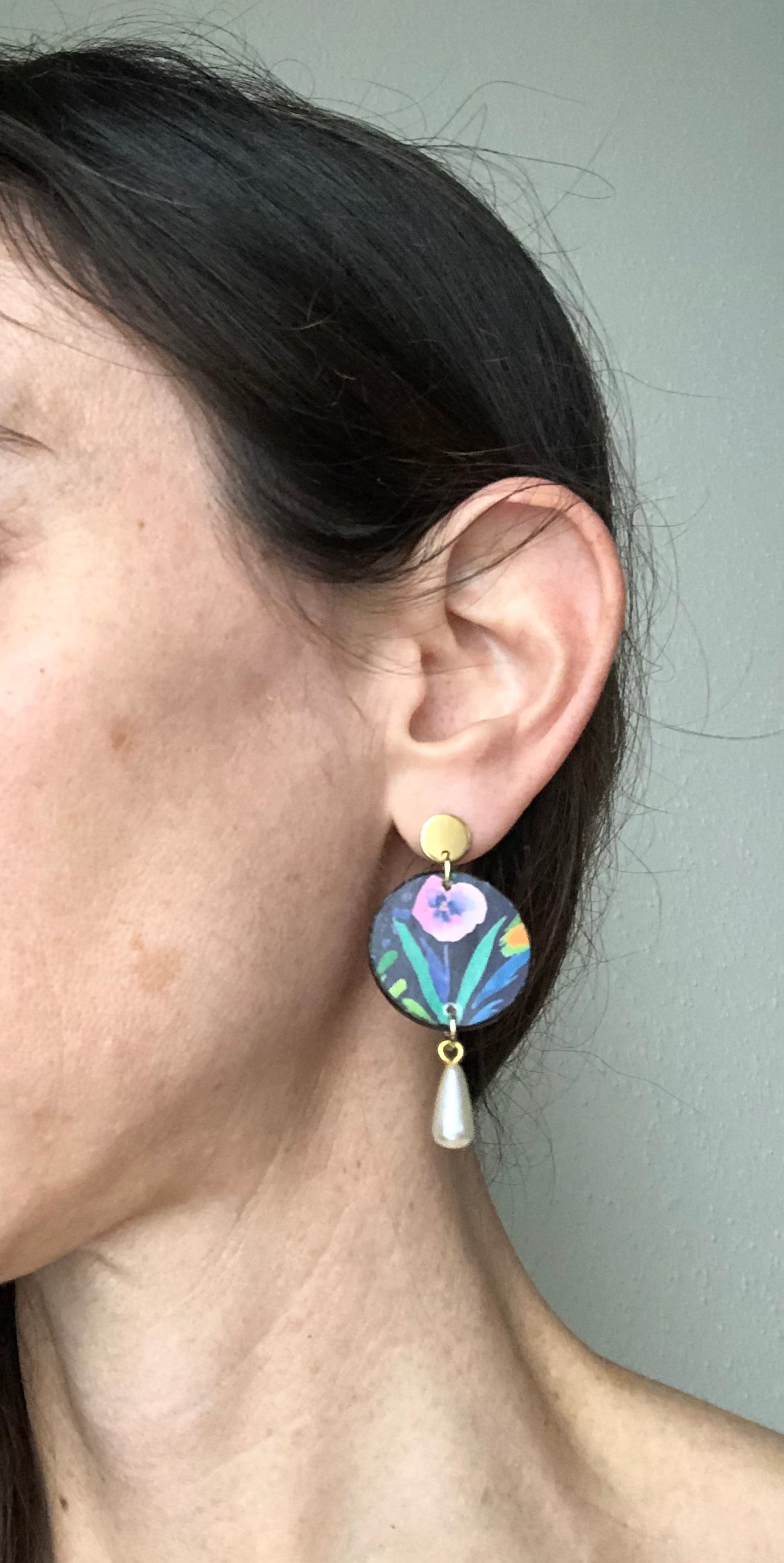 Close-up of a person wearing colorful earrings with a neutral background