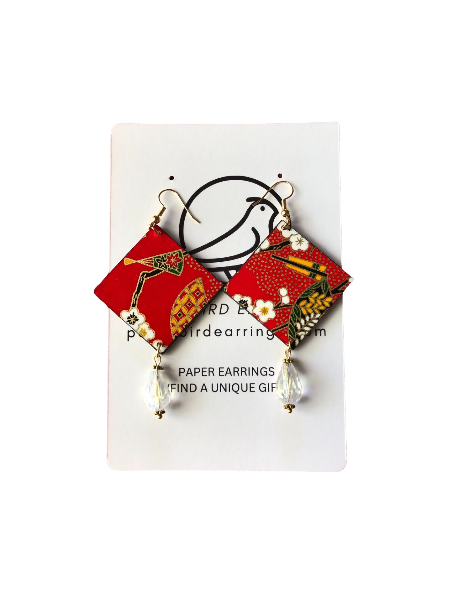Pair of red and gold patterned earrings on a white card with text.
