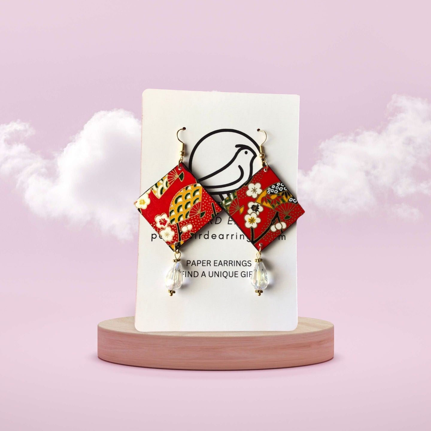 Decorative paper earrings on a white card with a pink background