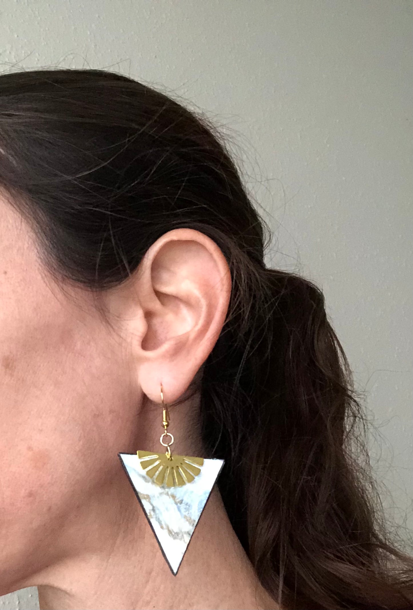 Person wearing a gold and white triangle earring with a plain background