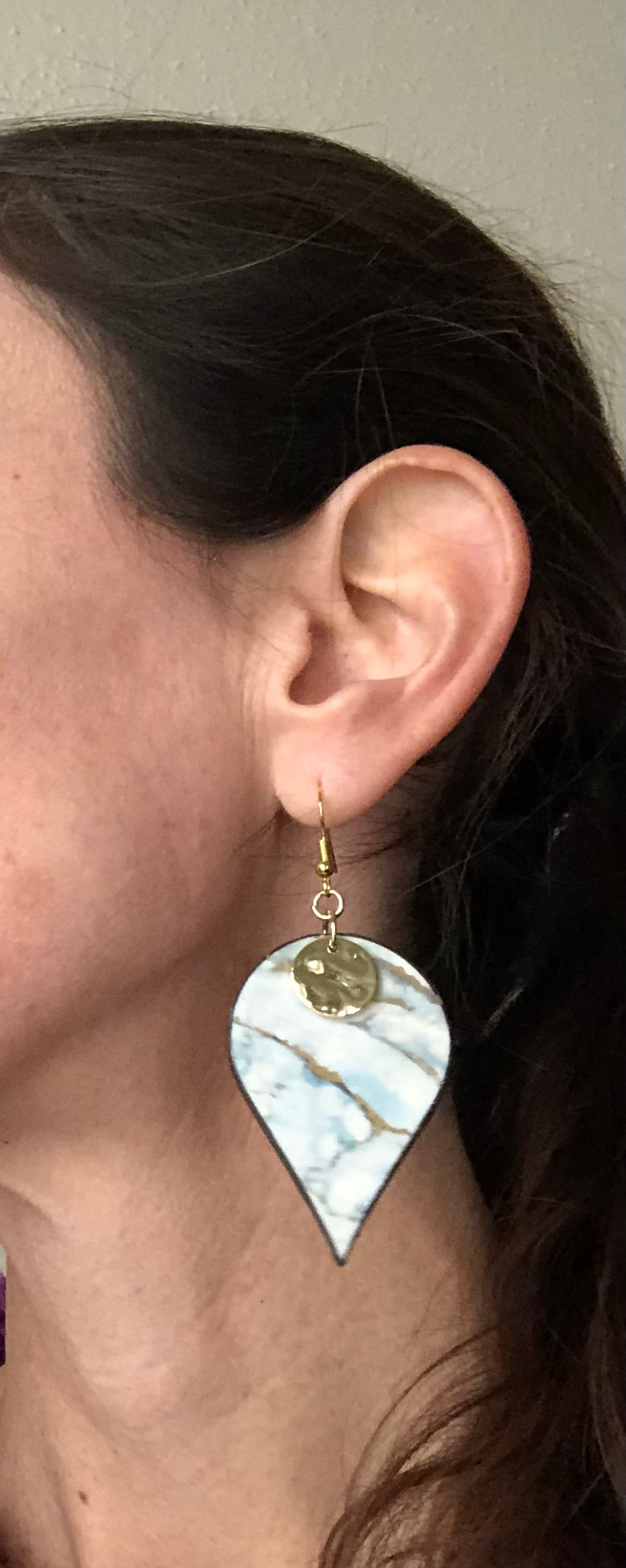 Person wearing a teardrop-shaped earring with a marbled design.