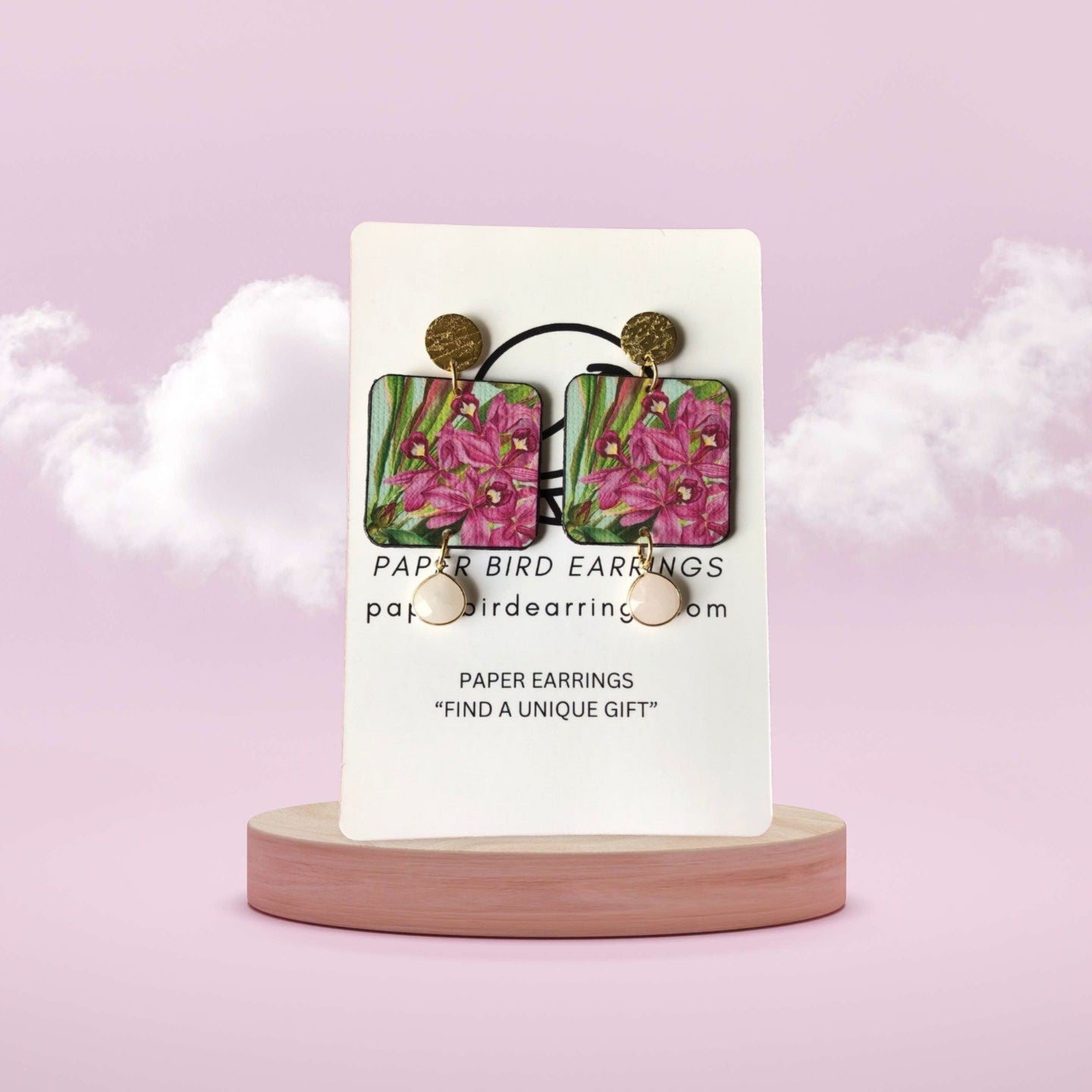 Paper bird earrings on a display card with a pink background
