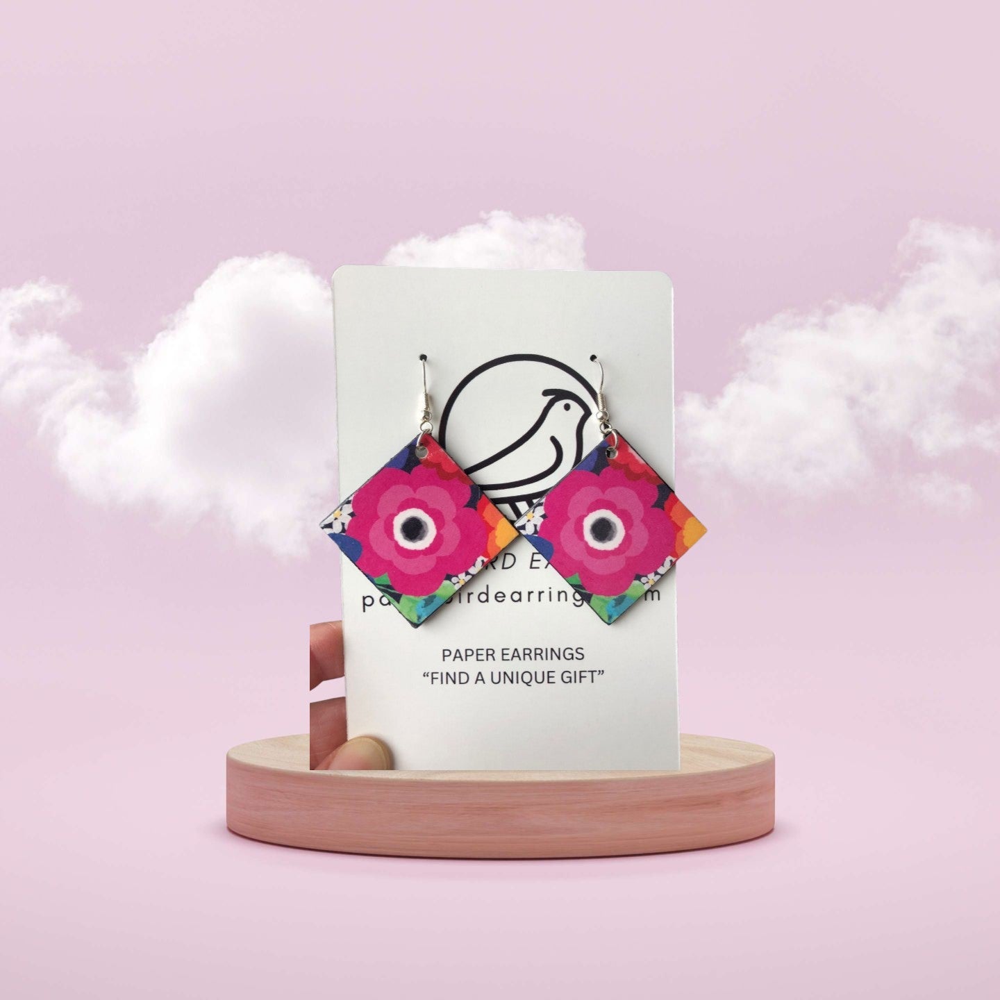 Colorful paper earrings on a white card with a pink background