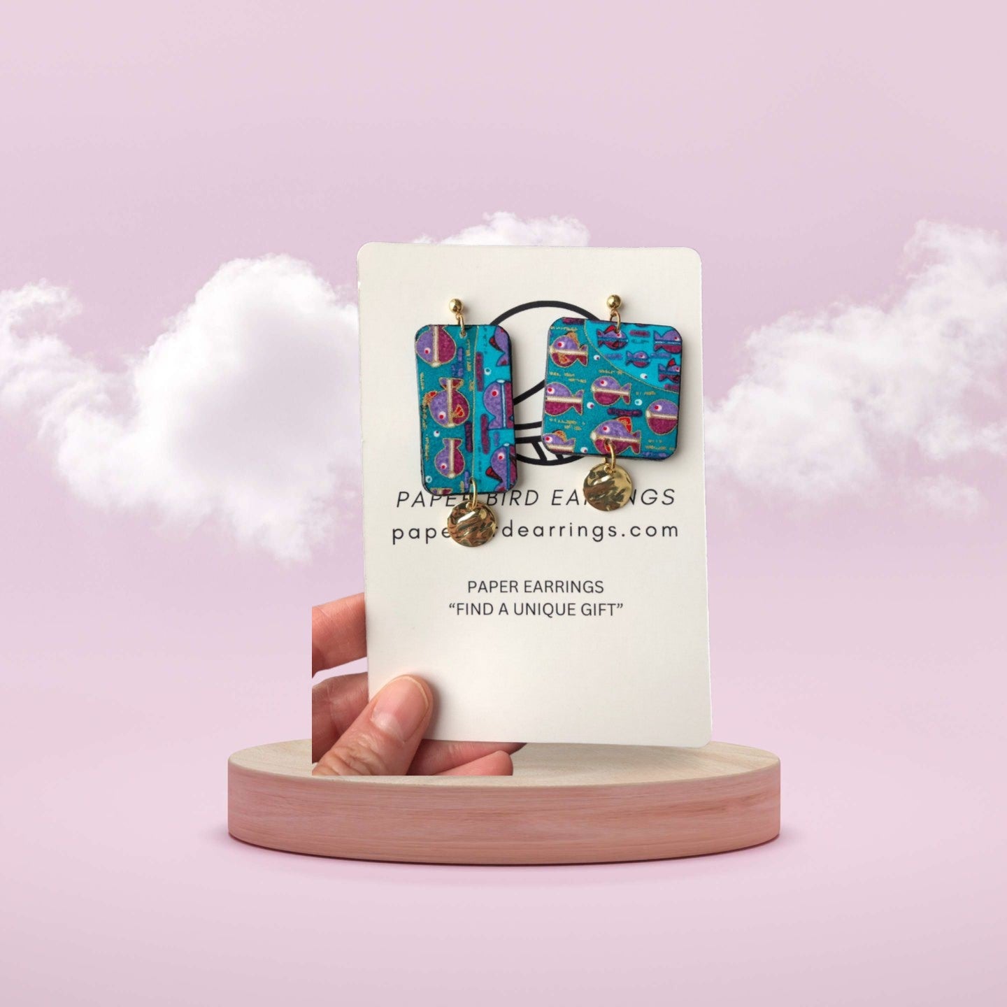 Hand holding a card with colorful earrings on a pink background