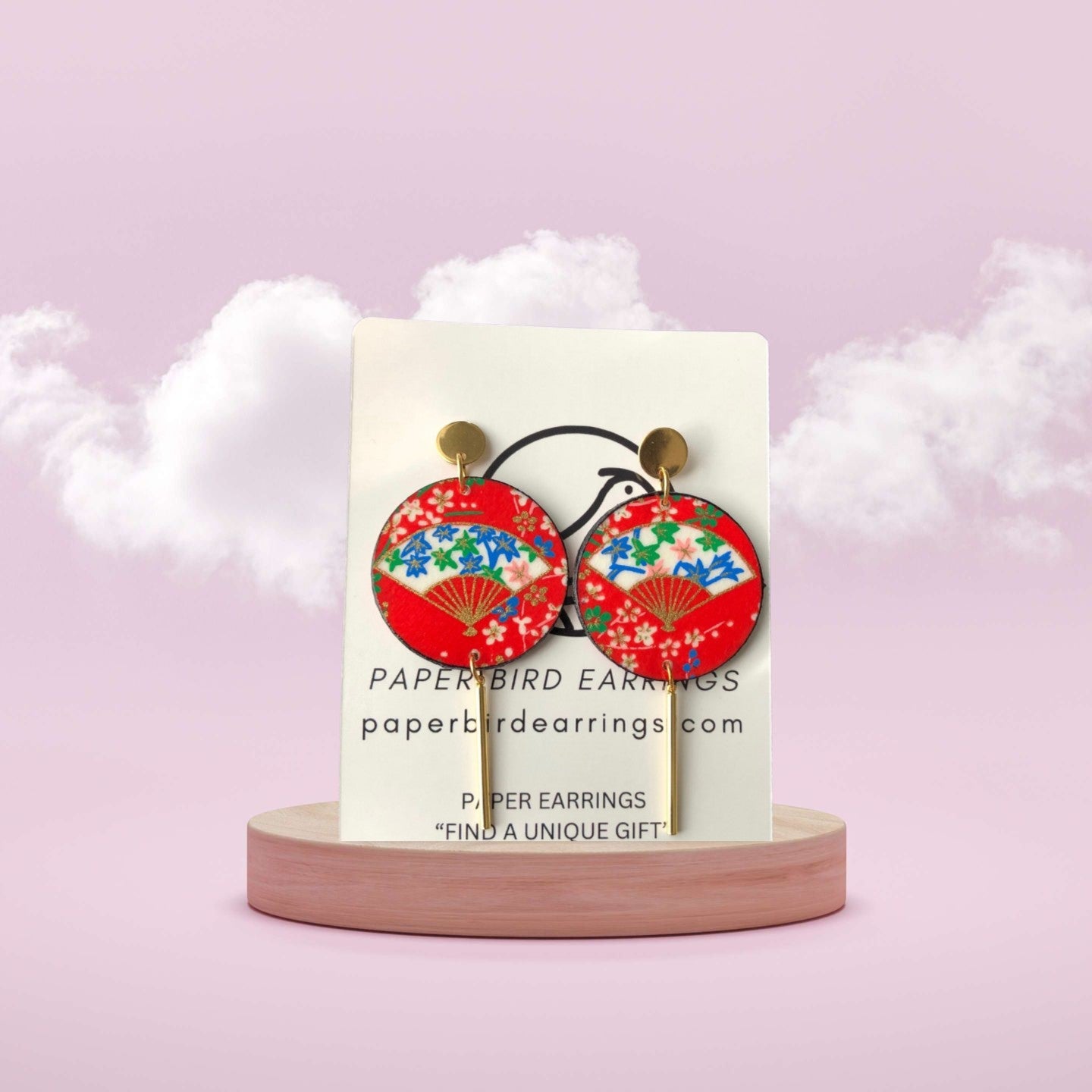 Red and gold paper earrings on a white card with 'Paperbird Earrings' branding against a pink background.