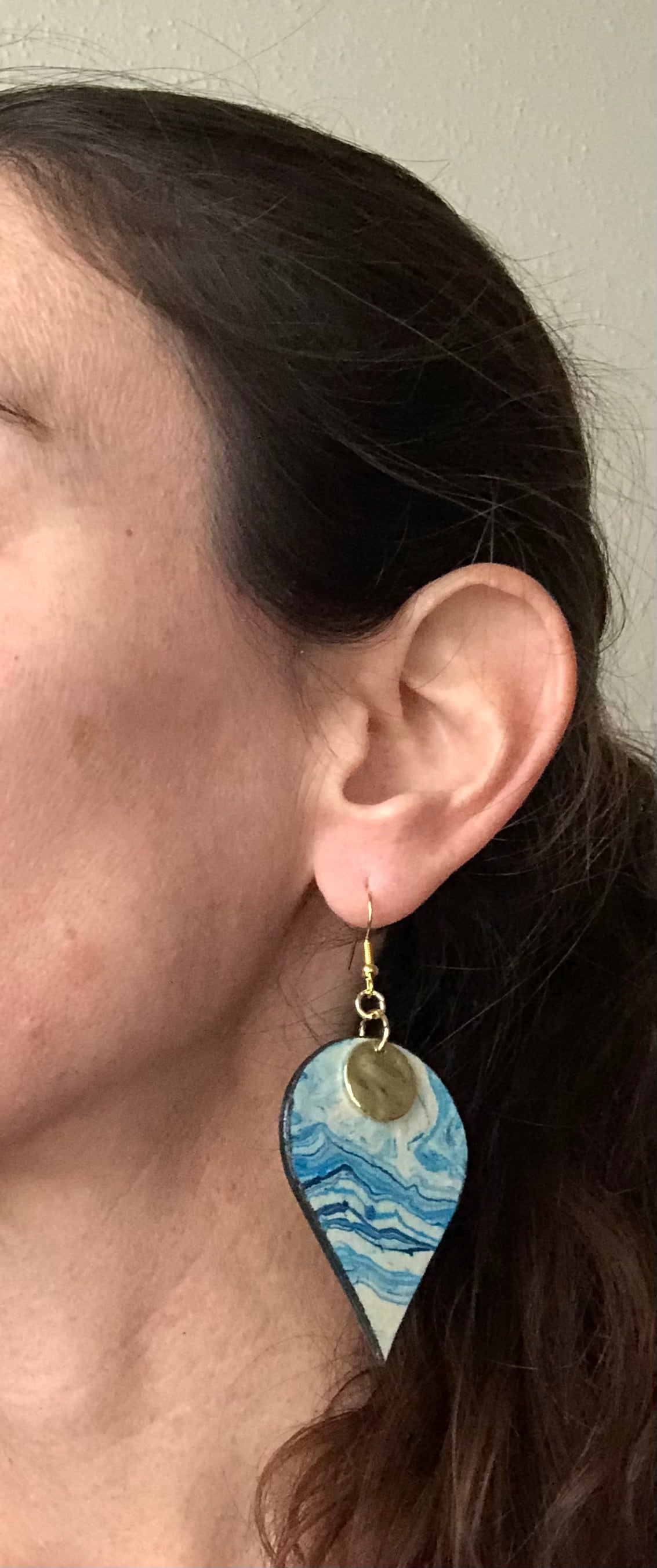 Close-up of a person wearing a blue and white earring with a gold accent.