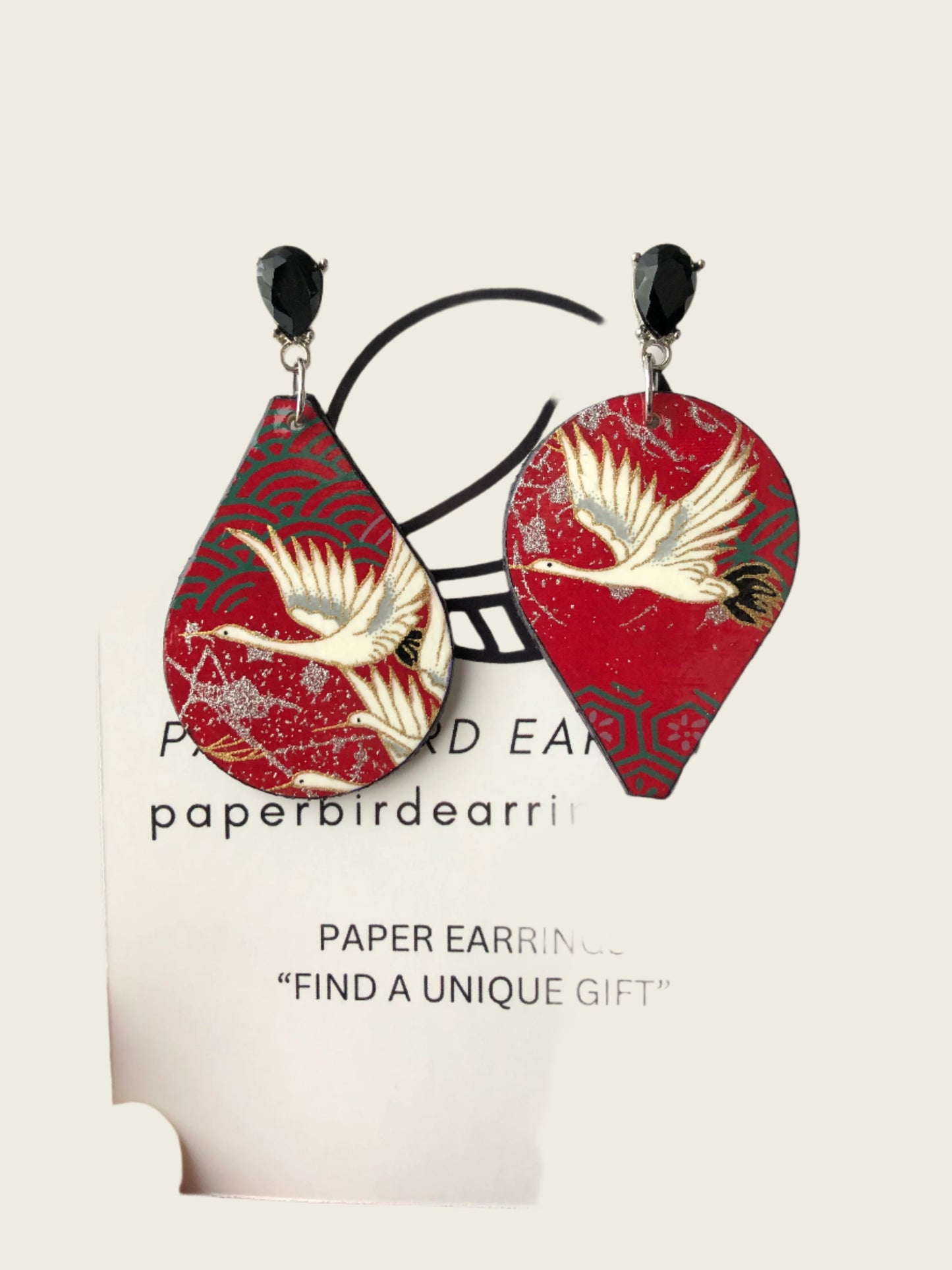 Red and white paper earrings on a display card with branding text.