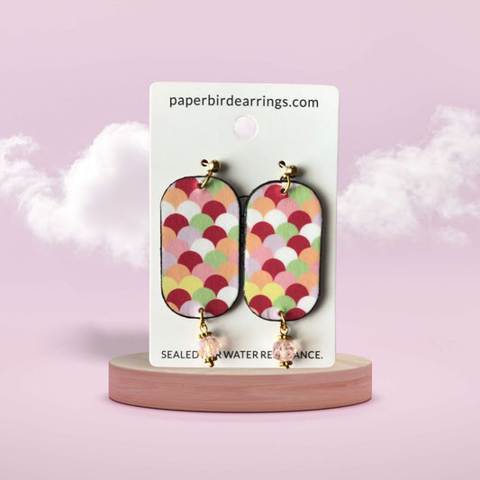 Colorful patterned earrings on a branded card with a pink background