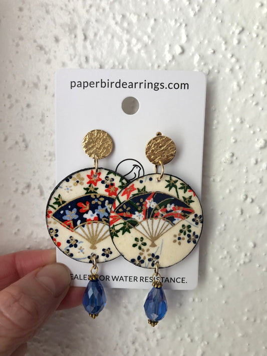 handmade paper earrings with blue bamboo fan on beige background with a round drop design with blue beads