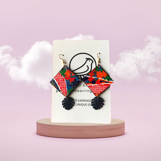 Colorful geometric earrings on a display card with a pink background