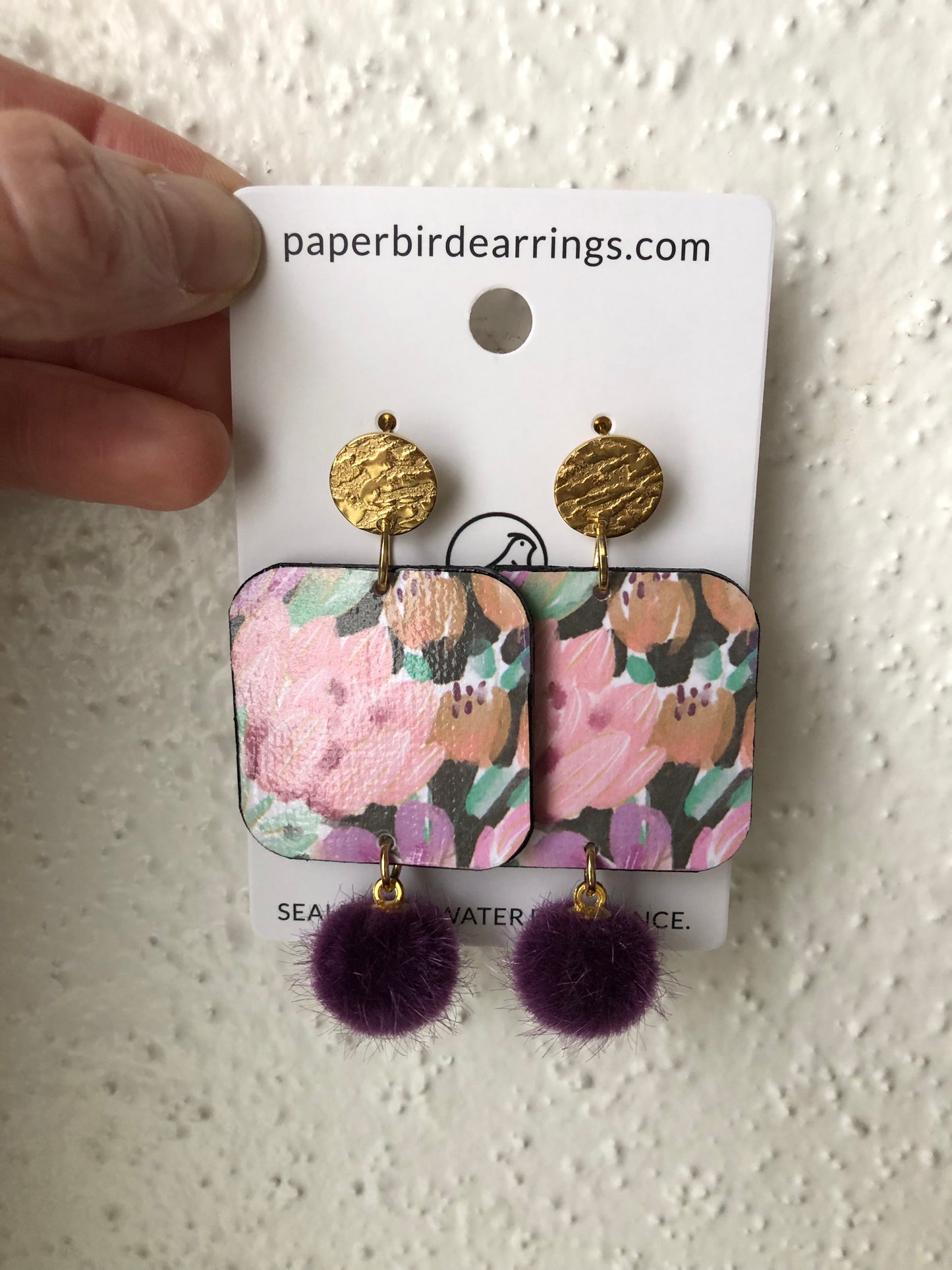 Pair of handmade paper earrings with floral coral flower design and purple pom-poms 
