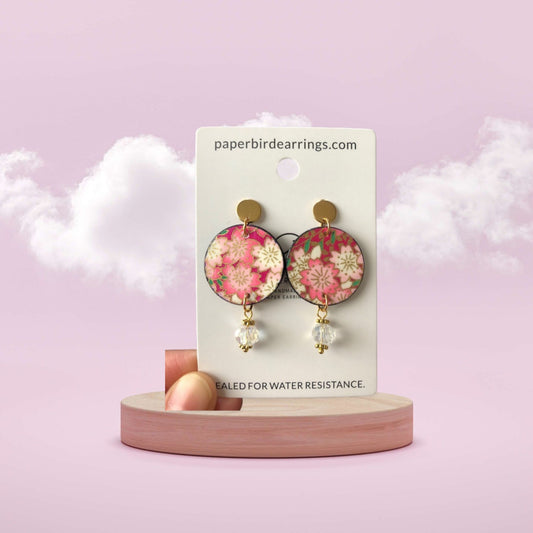 Floral earrings on a display card with a pink background
