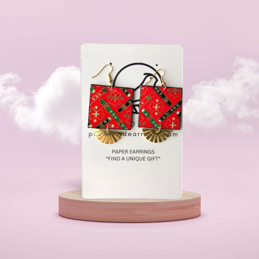 Red and gold paper earrings on a white card with a pink background