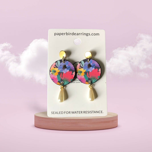 Colorful earrings on a branded card with a pink background