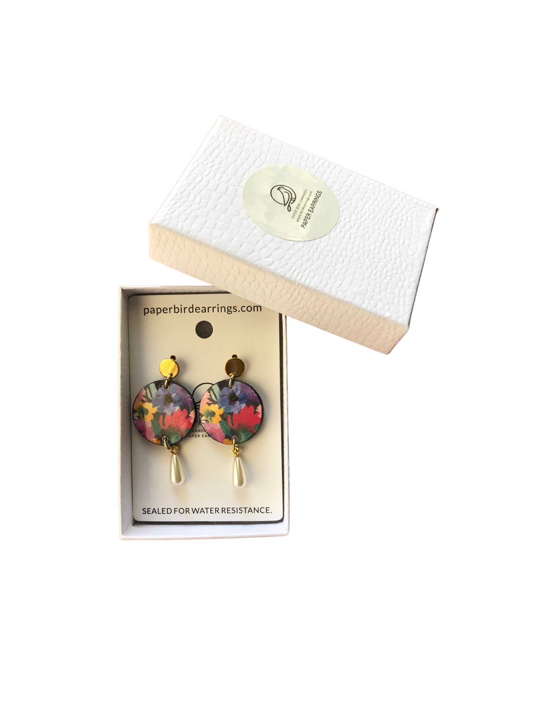 Colorful earrings in a box with a brand label on a white background