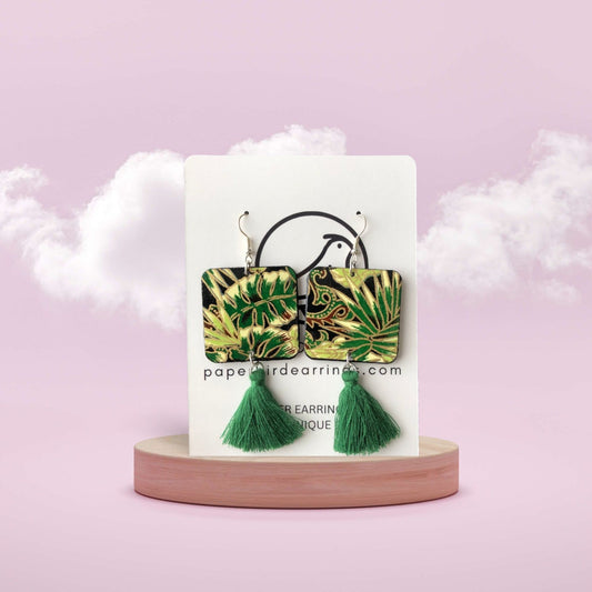 Green leaf-patterned earrings with tassels on a white card against a pink background