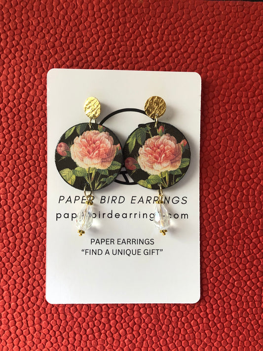 Handmade paper earrings with a Grandiflora rose design on a black background, displayed on a red textured surface.