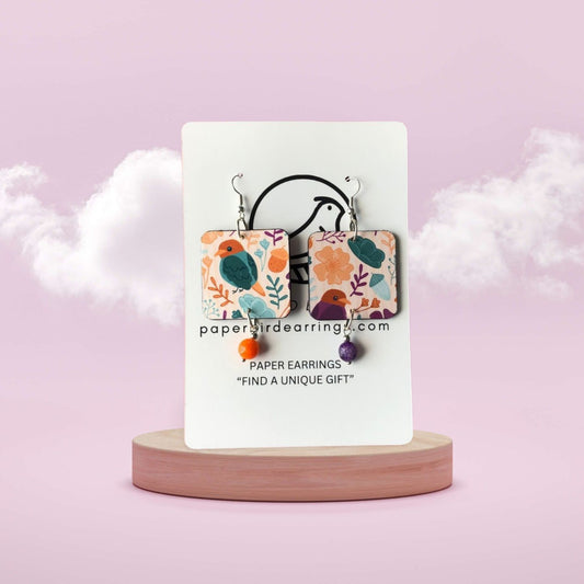 Pair of floral paper earrings on a display card with a pink background