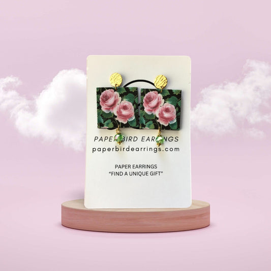 Card with floral earrings on a pink stand against a light purple background