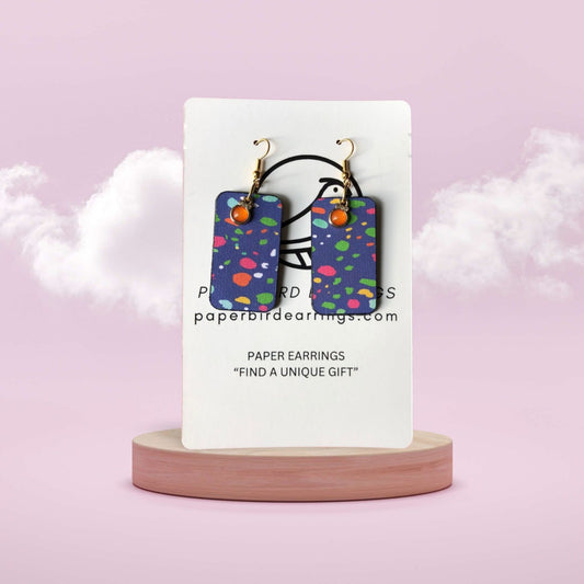 Colorful earrings on a white card with 'paperbirdearrings.com' text, against a pink background.