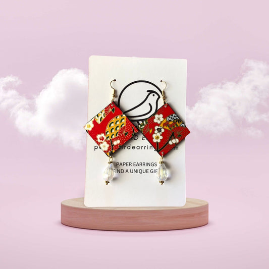 Decorative paper earrings on a white card with a pink background