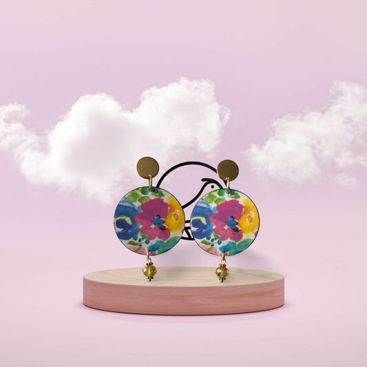 Colorful floral earrings on a wooden stand with a soft pink background