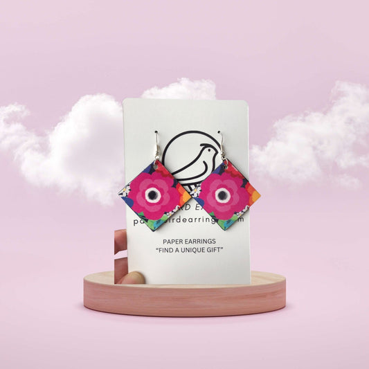 Colorful paper earrings on a white card with a pink background