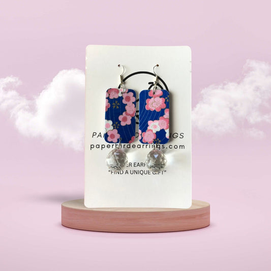 Floral earrings on a display card with a pink background
