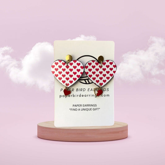 Heart-shaped paper earrings on a card with a pink background